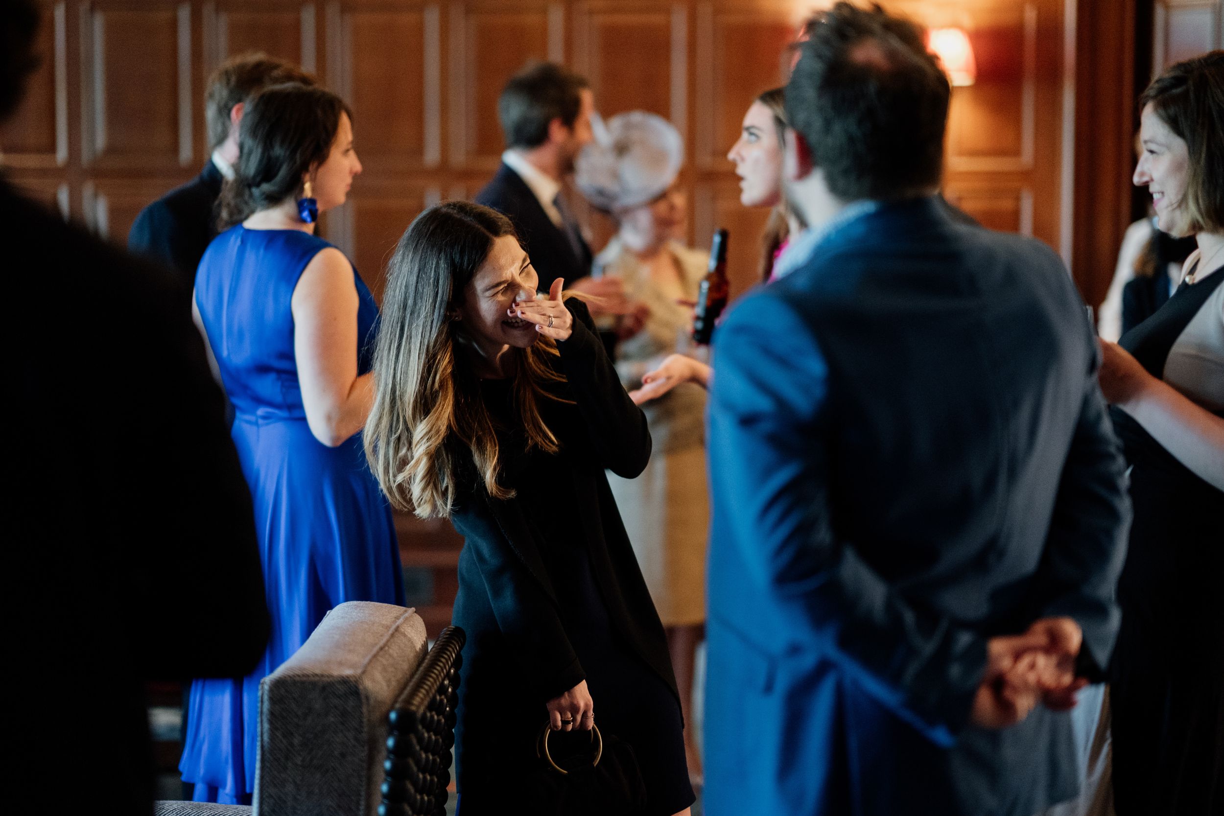 Wedding guests socializing at an evening reception in a wood-paneled room.