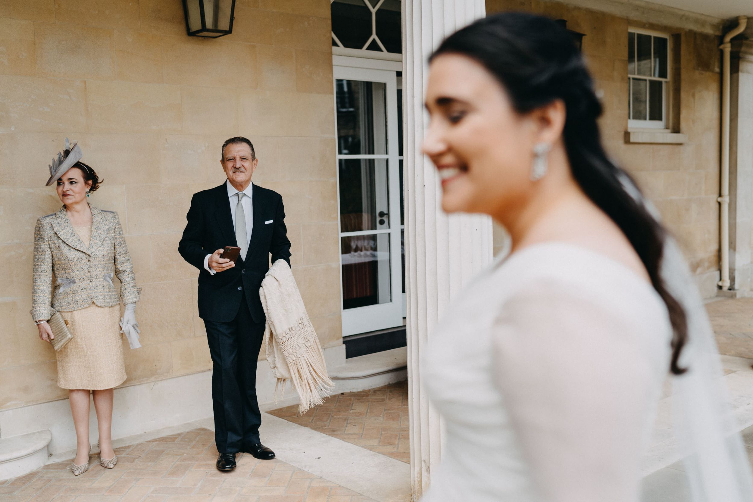 A wedding party gathers outside an elegant stone building with classic architecture.