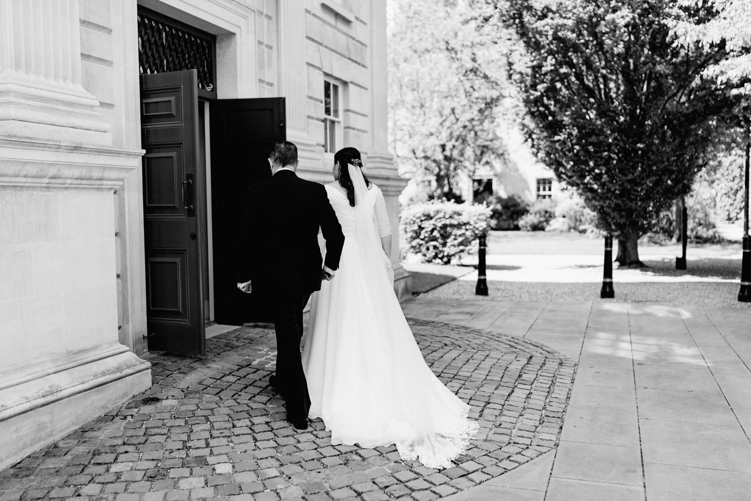 A couple enters a historic stone building on a cobblestone street during their wedding day.
