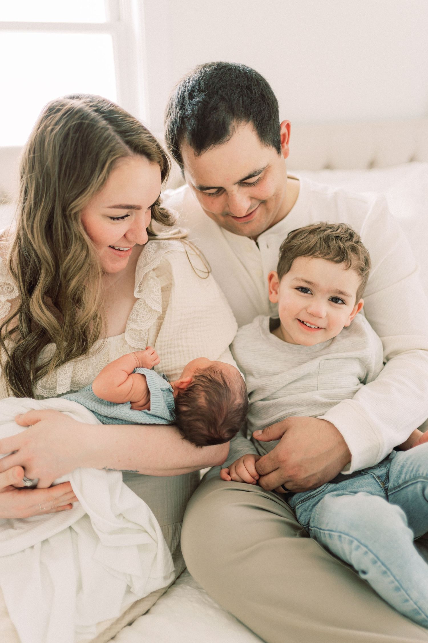 A family shares a tender moment on a white bed while bonding with their newborn baby.