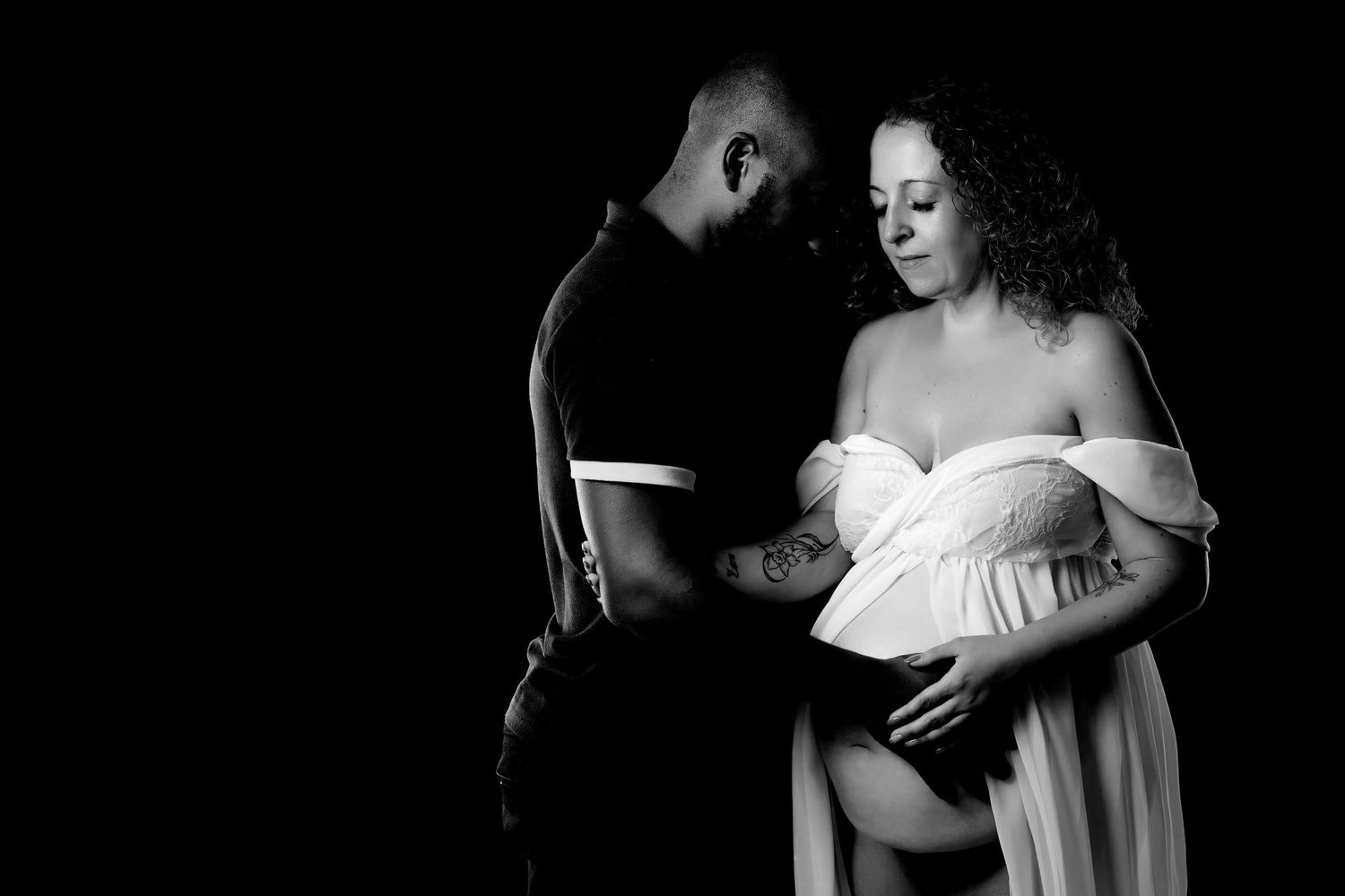 Black and white maternity photo featuring a couple sharing an intimate moment with the mother in a flowy dress.