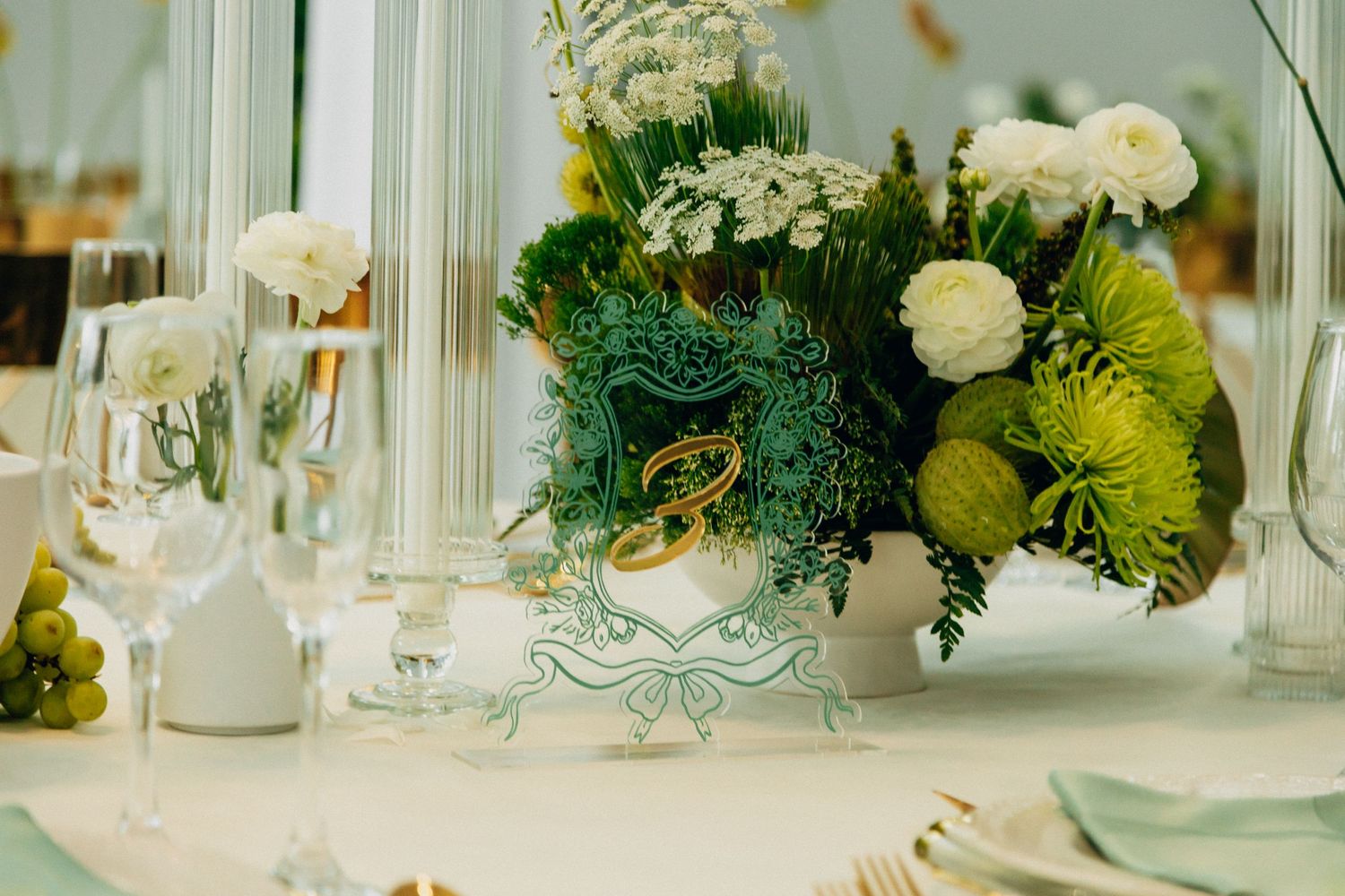 Luxurious wedding table centerpiece with white roses and greenery in an ornate white vase.