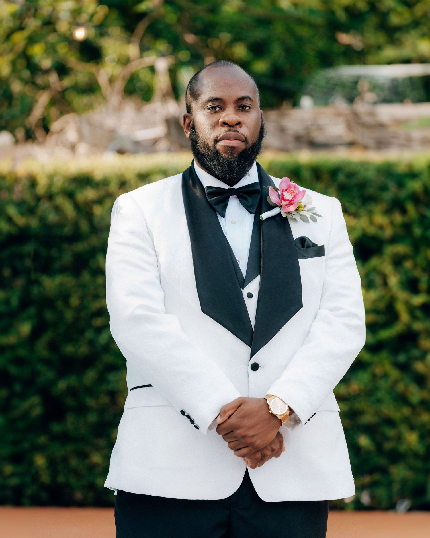 A groom in a white tuxedo jacket with black lapels and pink boutonniere poses for a formal portrait.