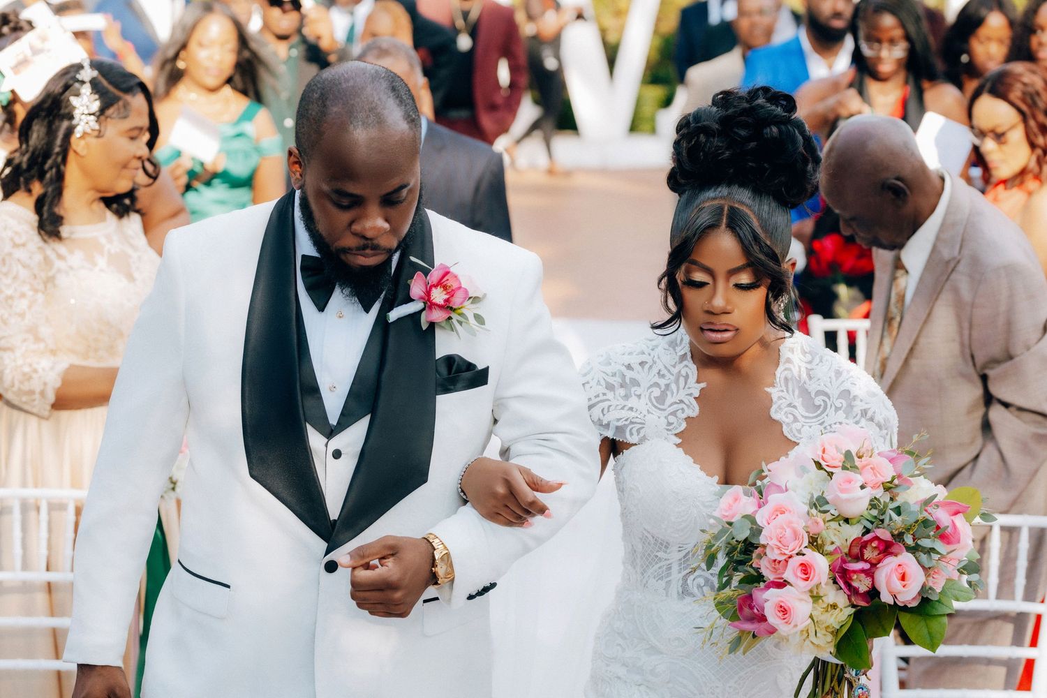 Wedding couple walking together in formal attire with bridal bouquet of pink flowers.