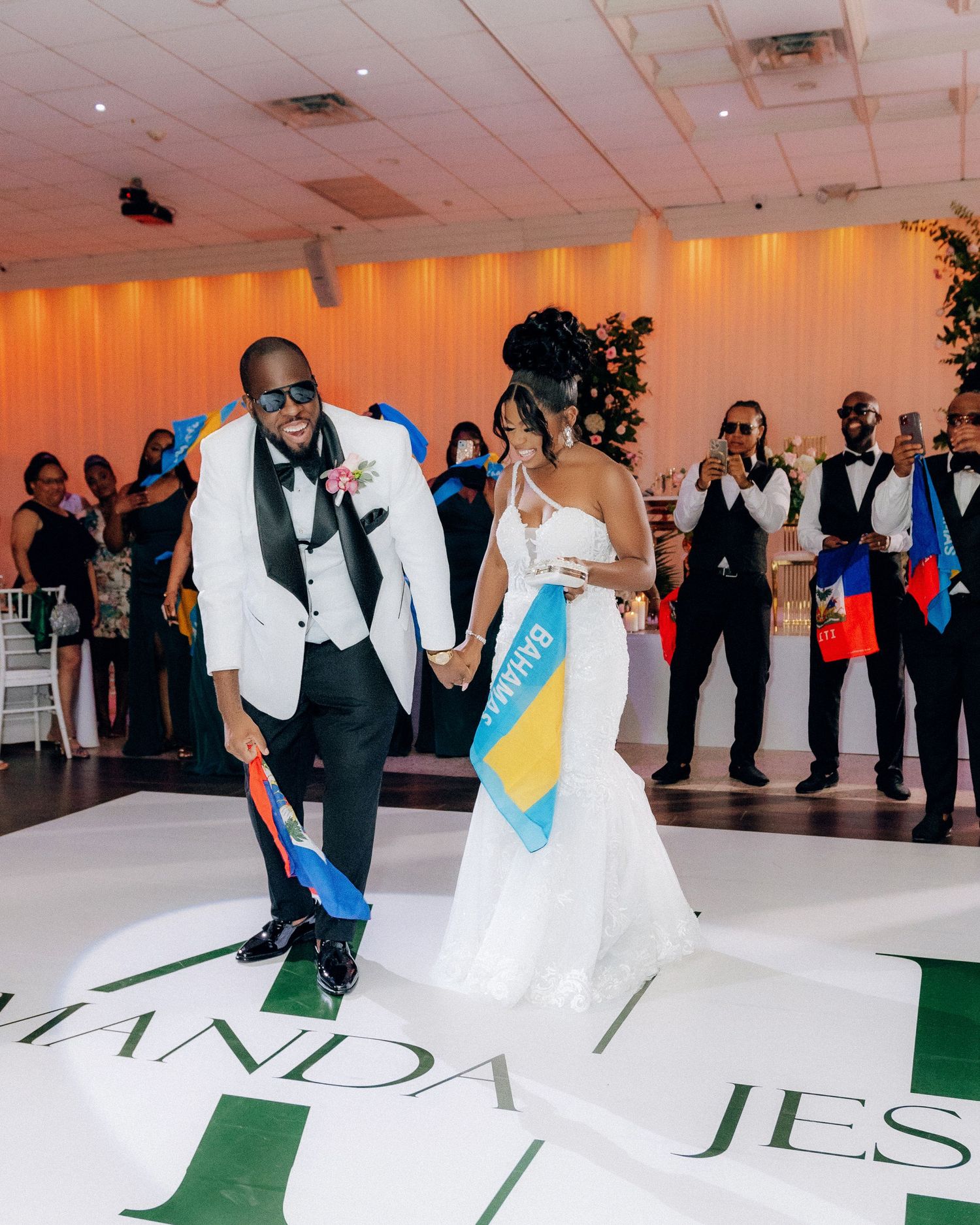 A couple wearing formal attire performs their first dance at a wedding reception with guests watching in background.