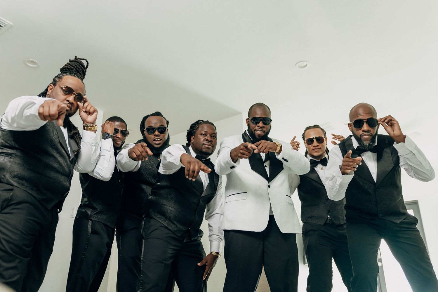 Groomsmen in black and white formal wear pose together making matching gestures.