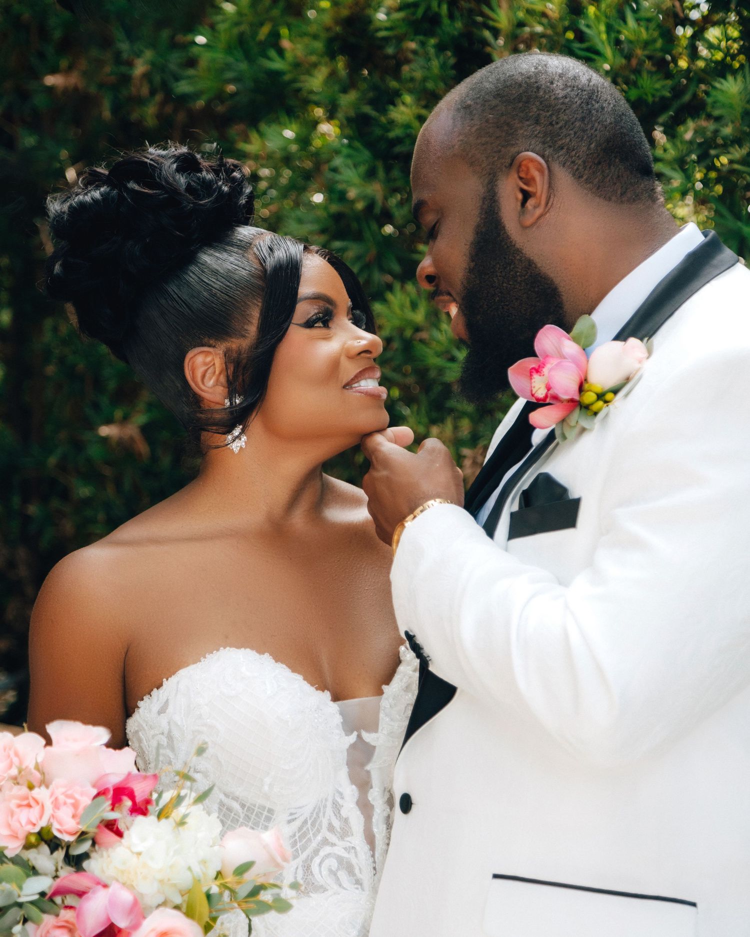 A tender moment between newlyweds in white attire against a garden backdrop.