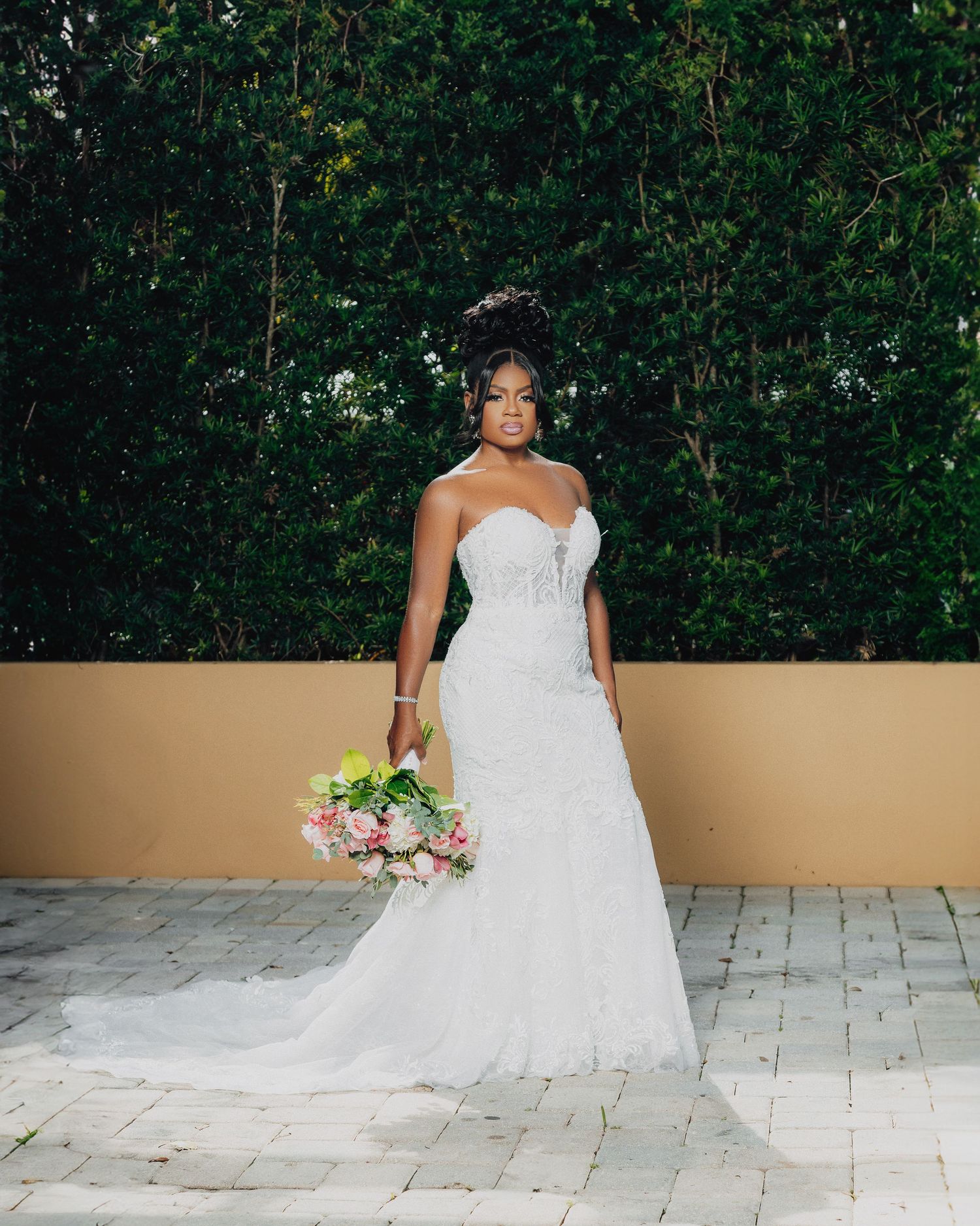 A bride in a stunning lace wedding gown poses with a pink and white bouquet.