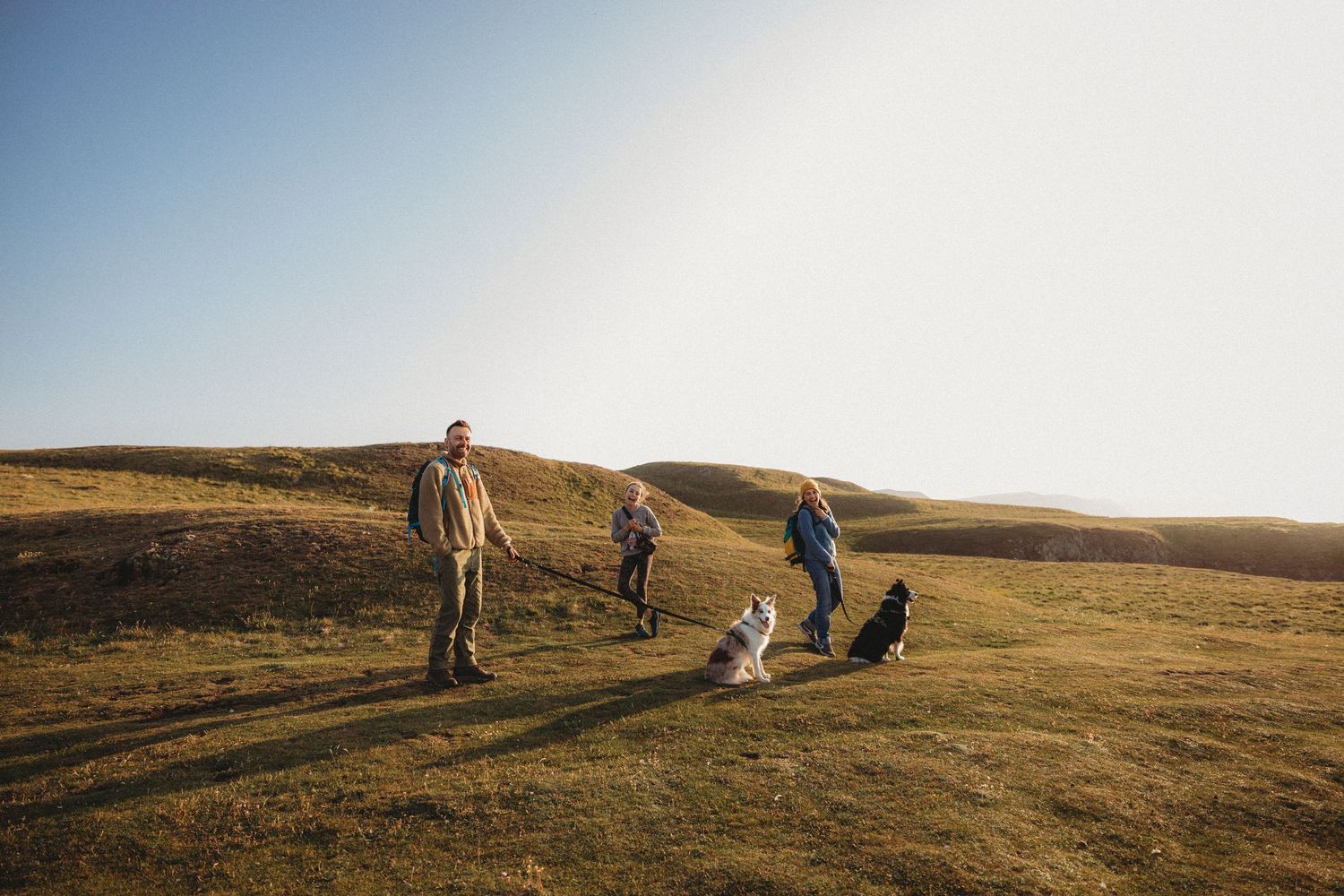Group explores rolling hills during golden hour as sun sets over picturesque landscape.