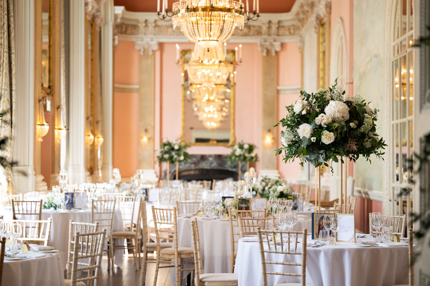Elegant ballroom wedding reception with crystal chandeliers, silver chiavari chairs and tall white floral centerpieces.