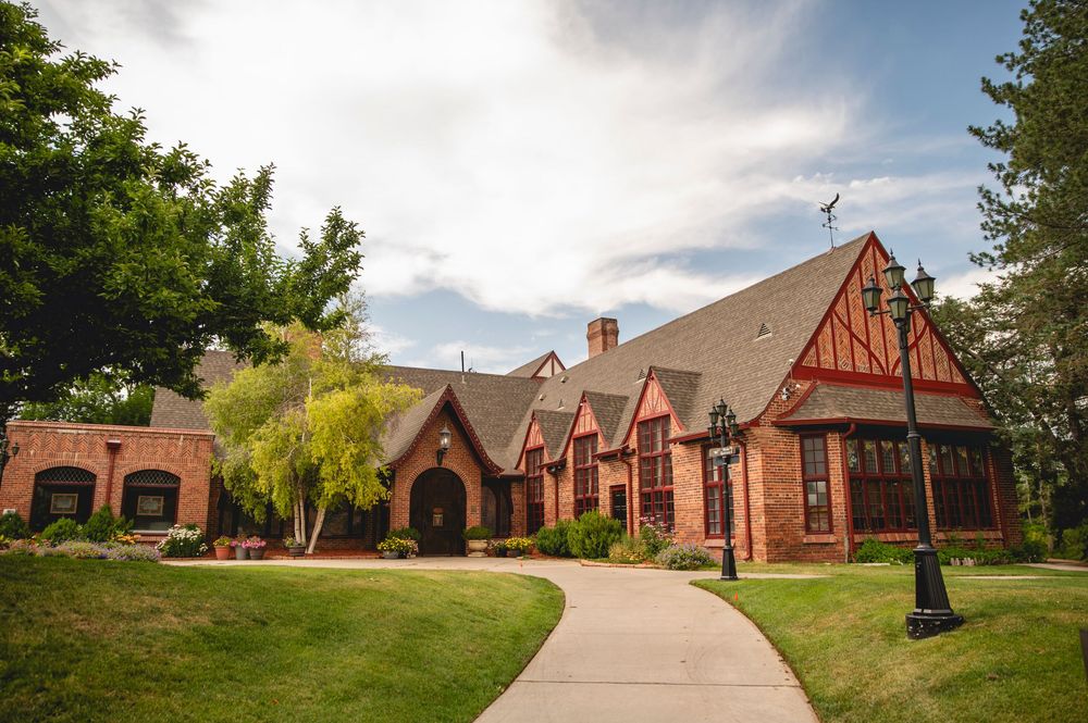 Red brick Tudor-style church building with multiple gabled entrances and a curved walkway through green lawn.