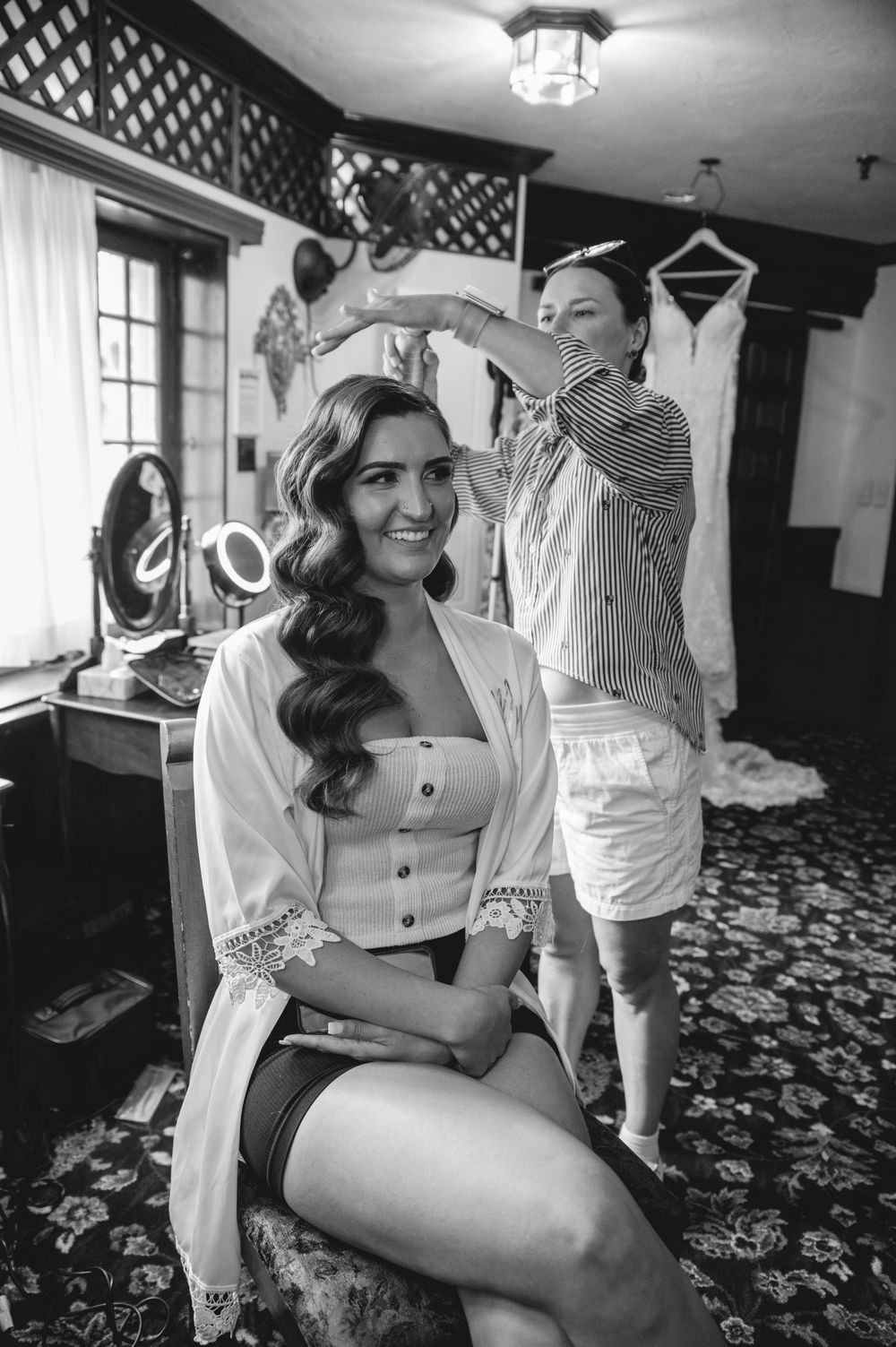 Black and white photo showing hair styling preparations in progress in a vintage dressing room setting.