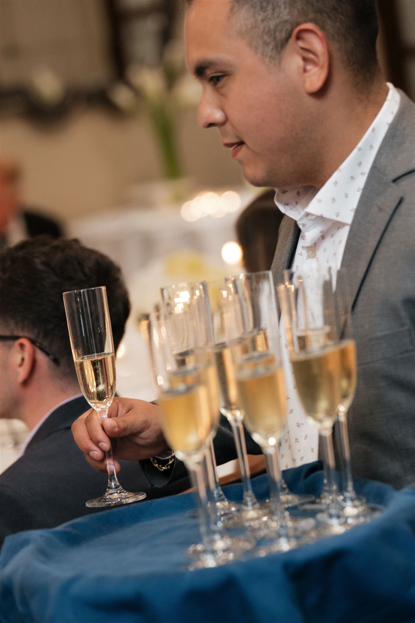 Row of champagne flutes filled with golden bubbles sits on a navy blue tablecloth at a formal event.
