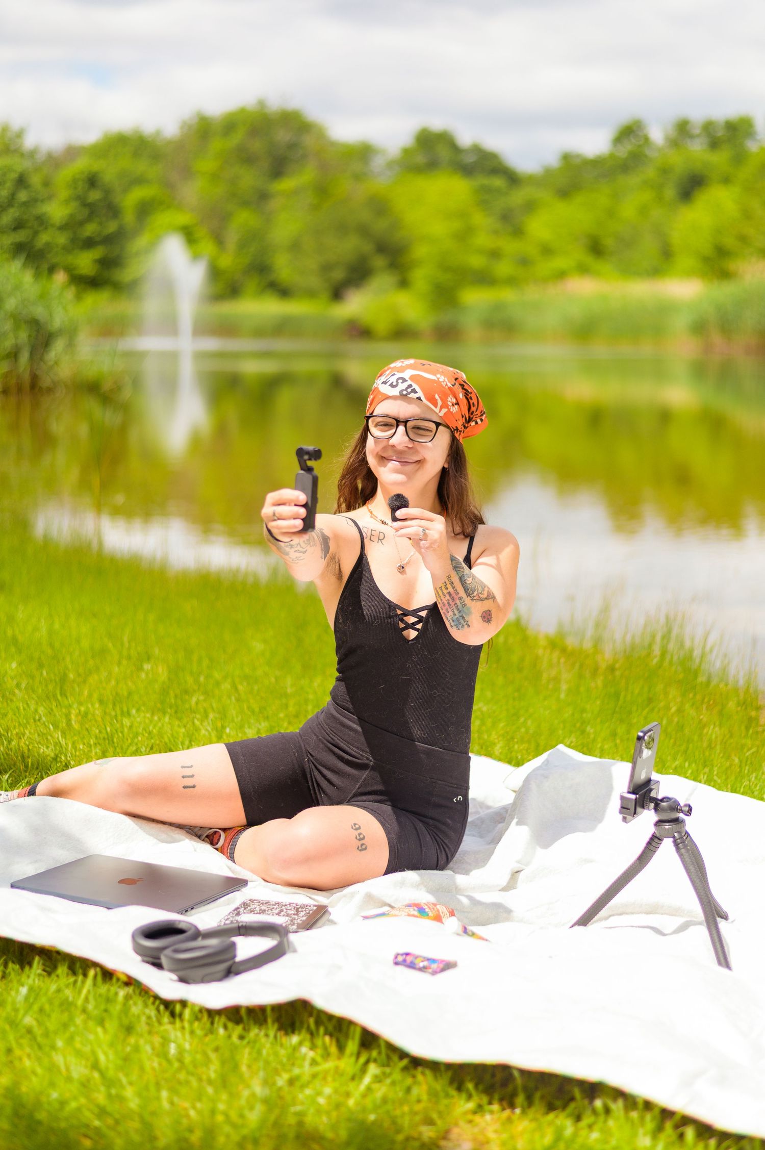 Person relaxes on white blanket by lake with photography equipment and laptop.
