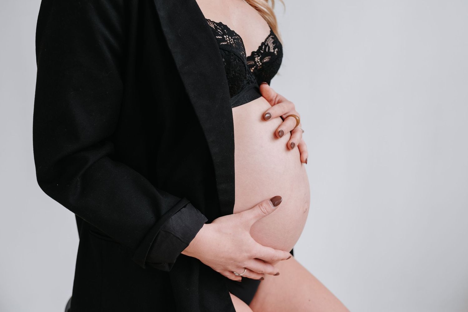 Pregnant person in black dress gently cradles belly during professional maternity photoshoot.