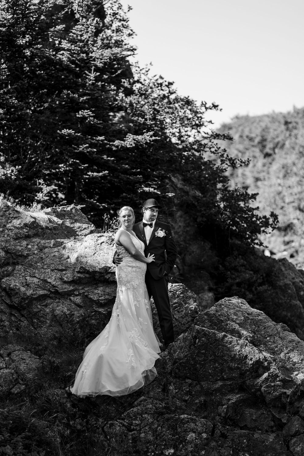 A black and white wedding photo captured on a rocky mountainside with trees in the background.