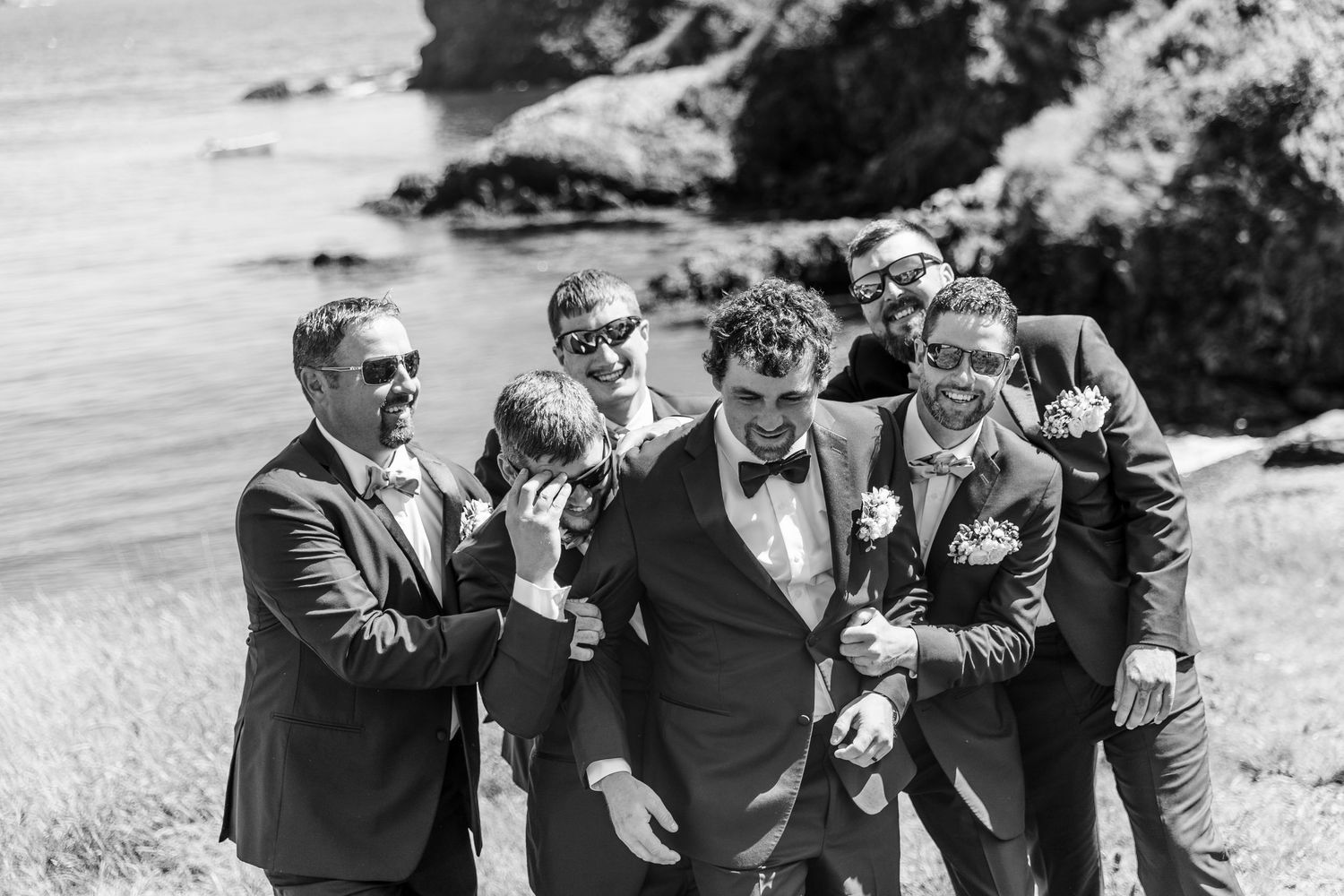 A black and white photo of groomsmen laughing together on a scenic coastal cliff.