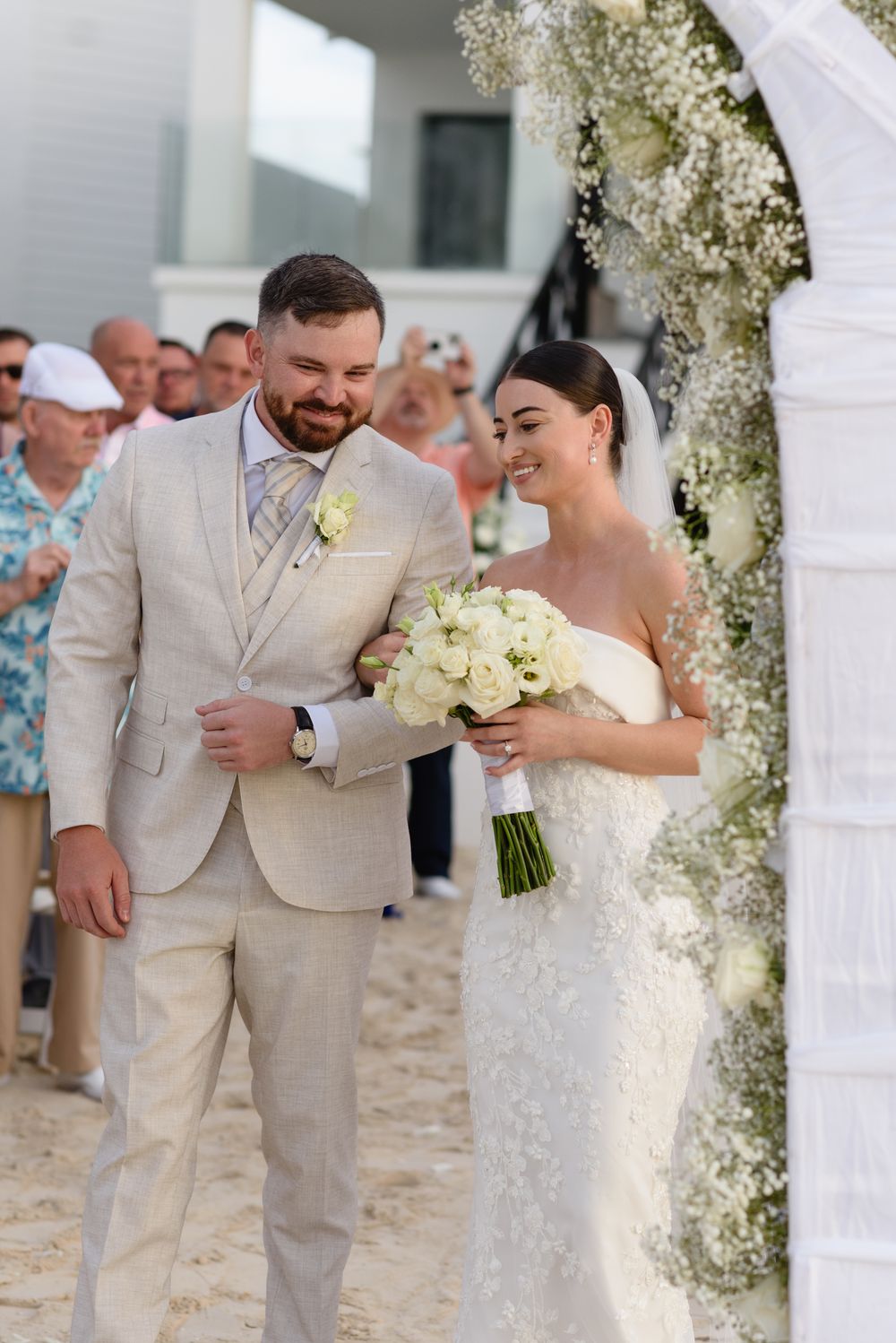 A wedding ceremony under an arch decorated with white flowers as the newlyweds share a joyful moment.