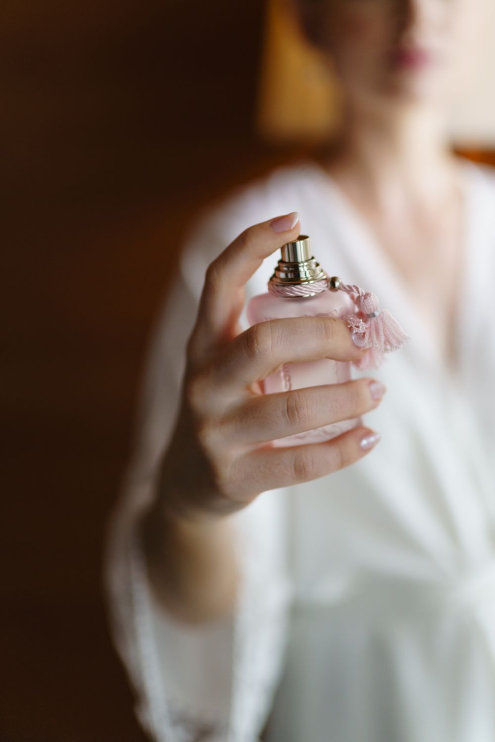 A delicate hand sprays perfume from an elegant glass bottle against a soft, blurred background.