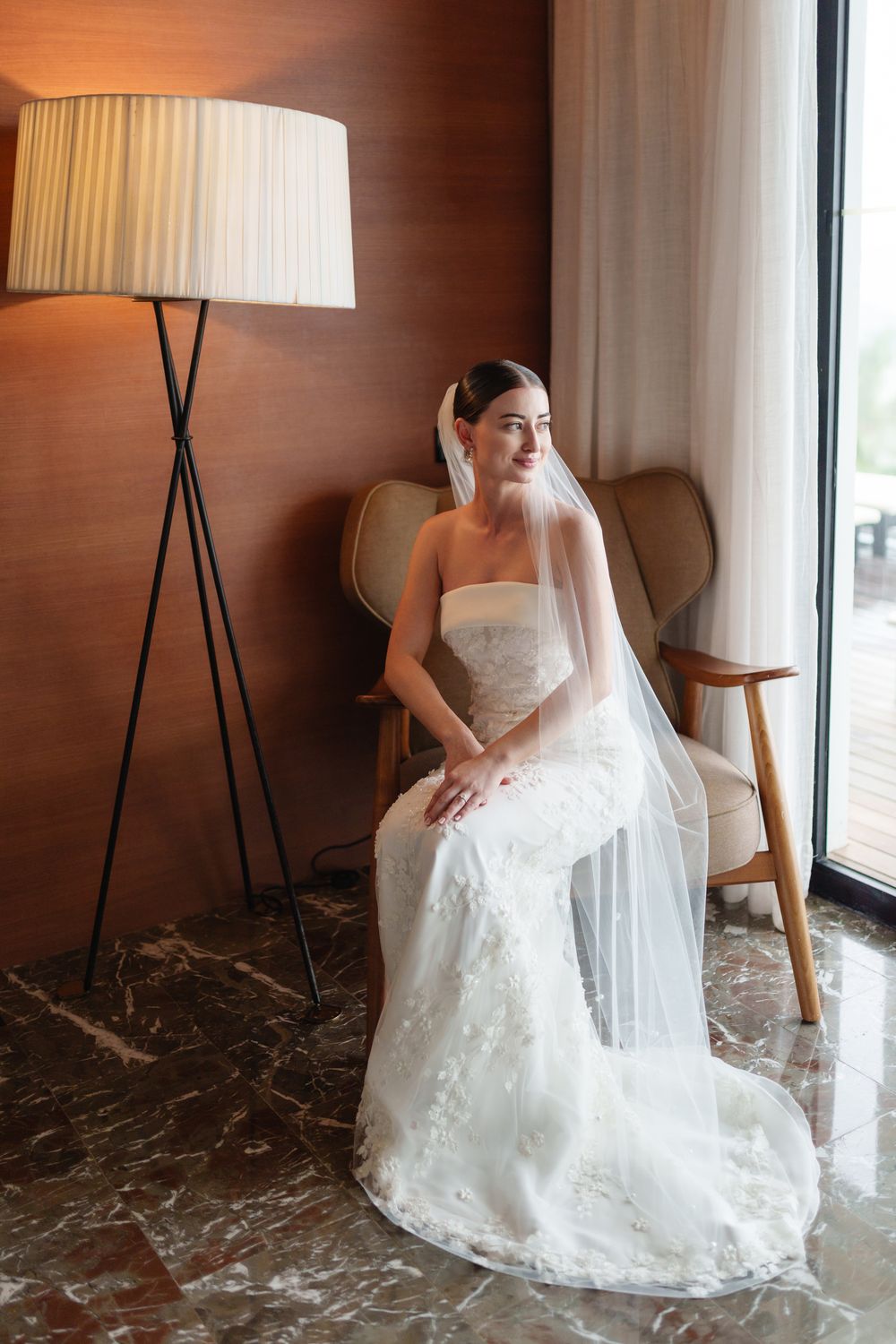 A bride in a white lace wedding dress sits elegantly by a window in a series of four similar poses.