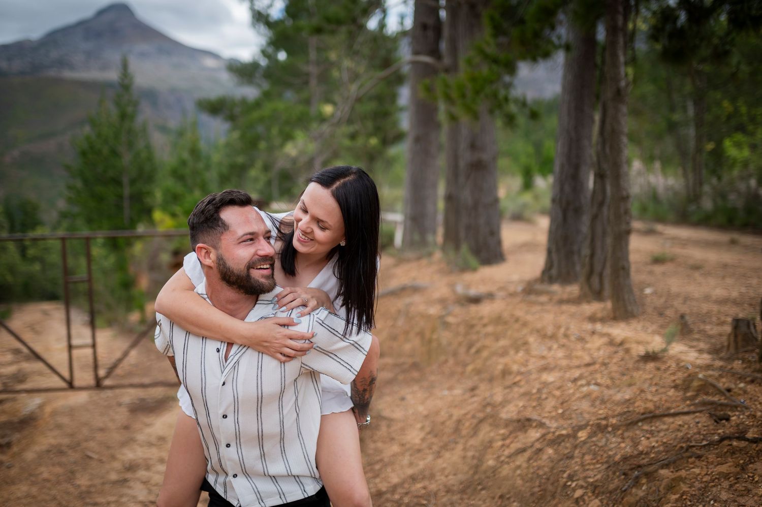 A romantic couple shares tender moments together while sitting in a mountainous forest setting during a photo session.