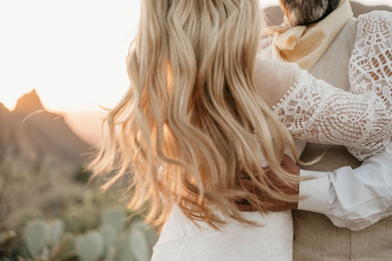 Close up detail of flowing blonde hair and lace wedding dress sleeve backlit by golden sunlight.