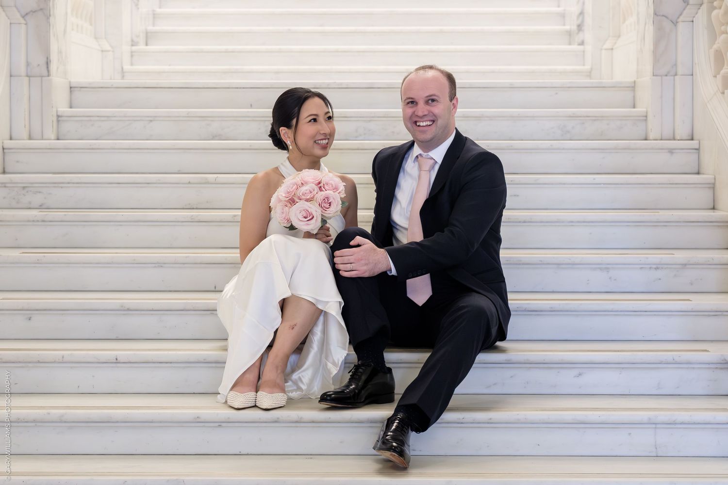 A couple in wedding attire sits together on white marble stairs in a series of romantic poses.