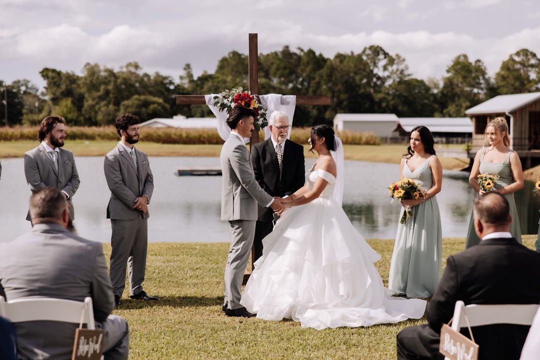 An outdoor wedding ceremony takes place beside a serene lake with white chairs and wedding decorations set up on the grass.