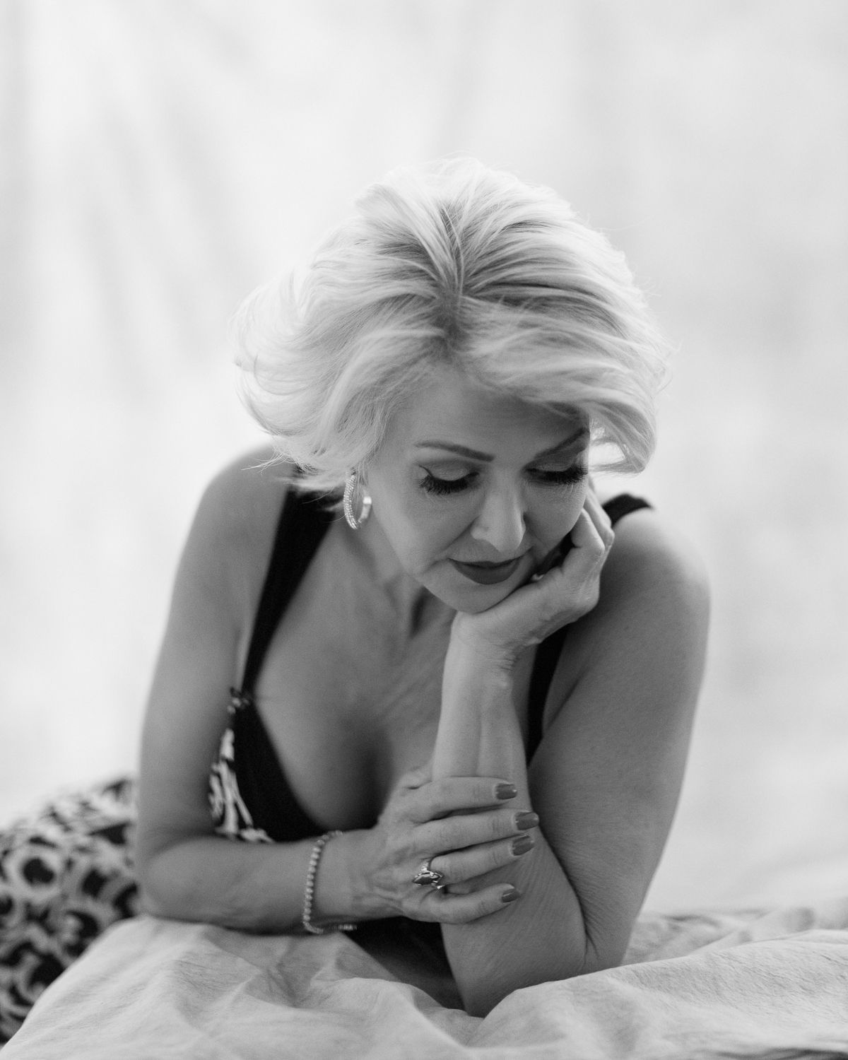 Black and white portrait of someone reclining on white fabric in casual pose with closed eyes and gentle smile.