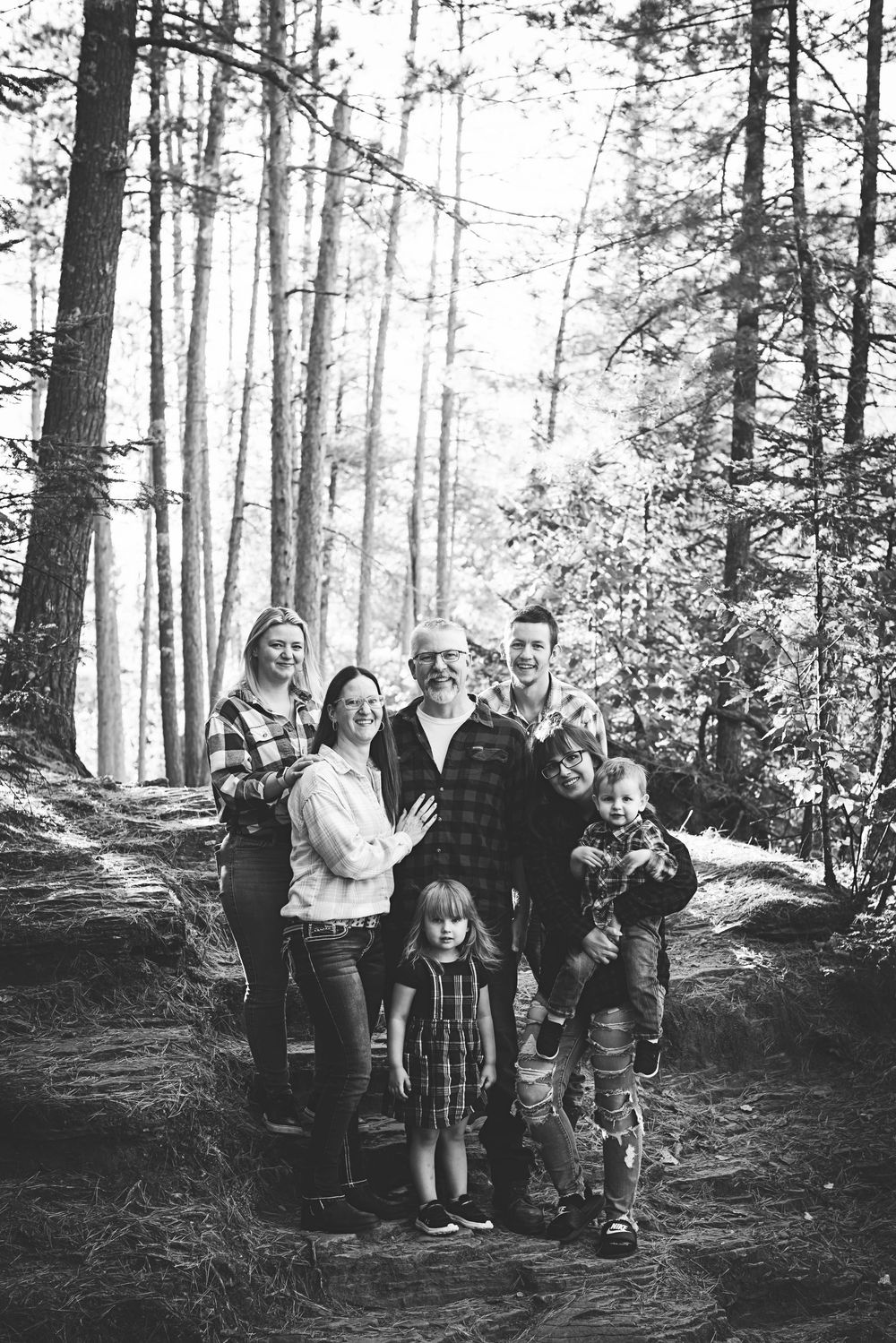 A group of people gathered together on a forest trail surrounded by tall trees in a black and white photo series.