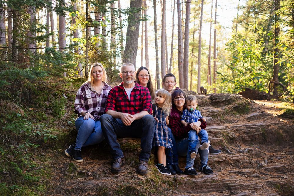 Group enjoying a moment together while sitting on a hillside trail in a sunny forest setting.