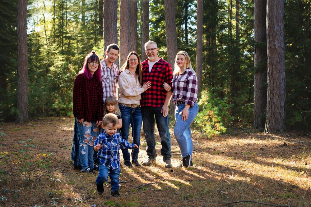 Family portrait session in a sunlit forest with multiple people wearing flannel and denim in autumn.