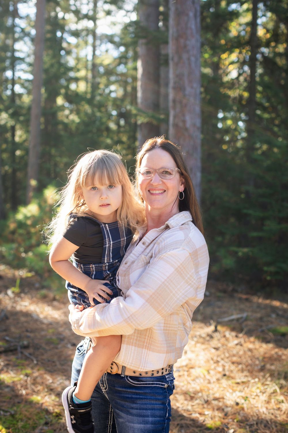 A heartwarming outdoor portrait of two people embracing and smiling in a sunlit forest setting.