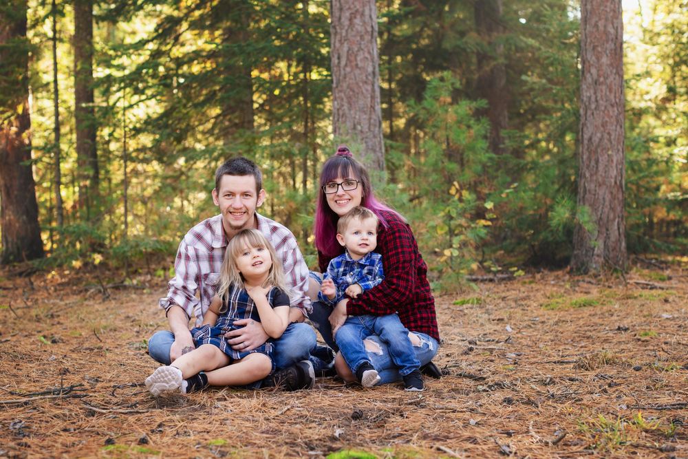 Family sitting together among pine trees on a forest floor covered in fallen needles during autumn.