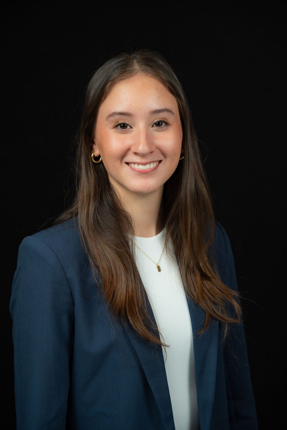 Professional headshot of a smiling person wearing a navy blazer and white top against a black background.