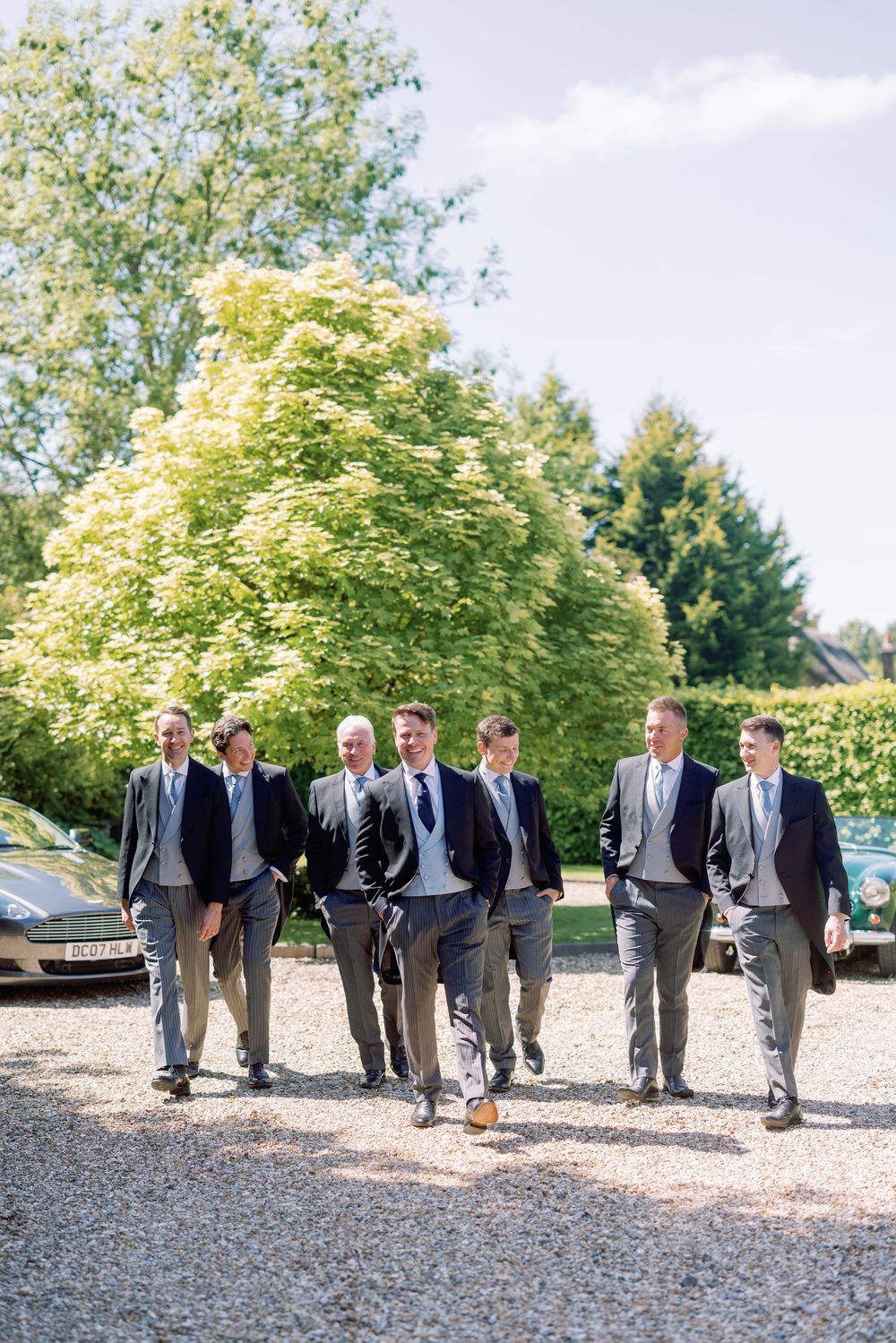 A group of groomsmen in matching gray suits walking together on a gravel path with trees in the background.