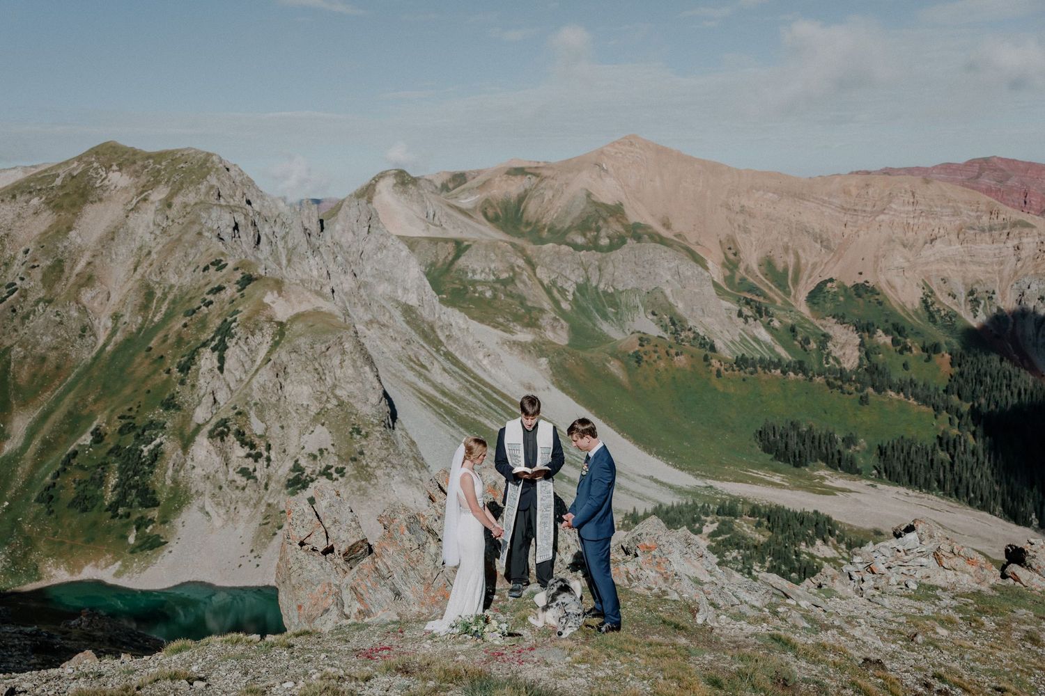 Two people stand together on a scenic mountain ridge overlooking rugged alpine peaks in the Colorado wilderness.