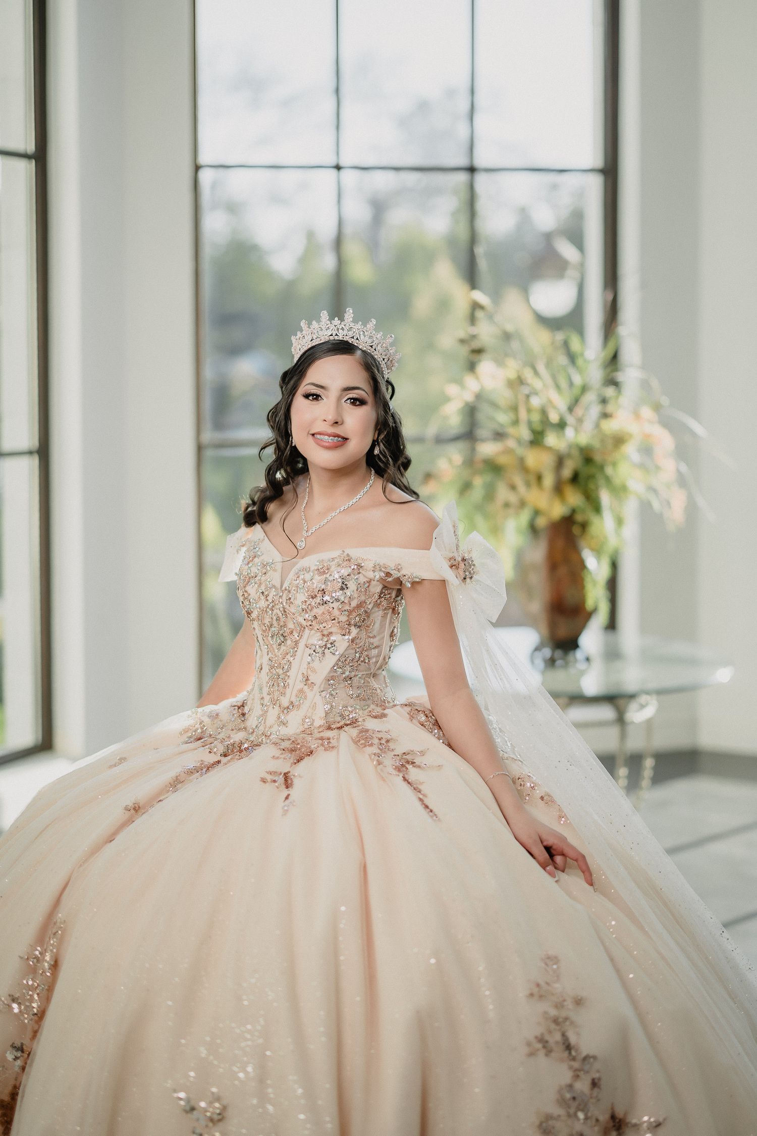 An off-shoulder champagne ballgown with delicate beading and lace details in natural light.