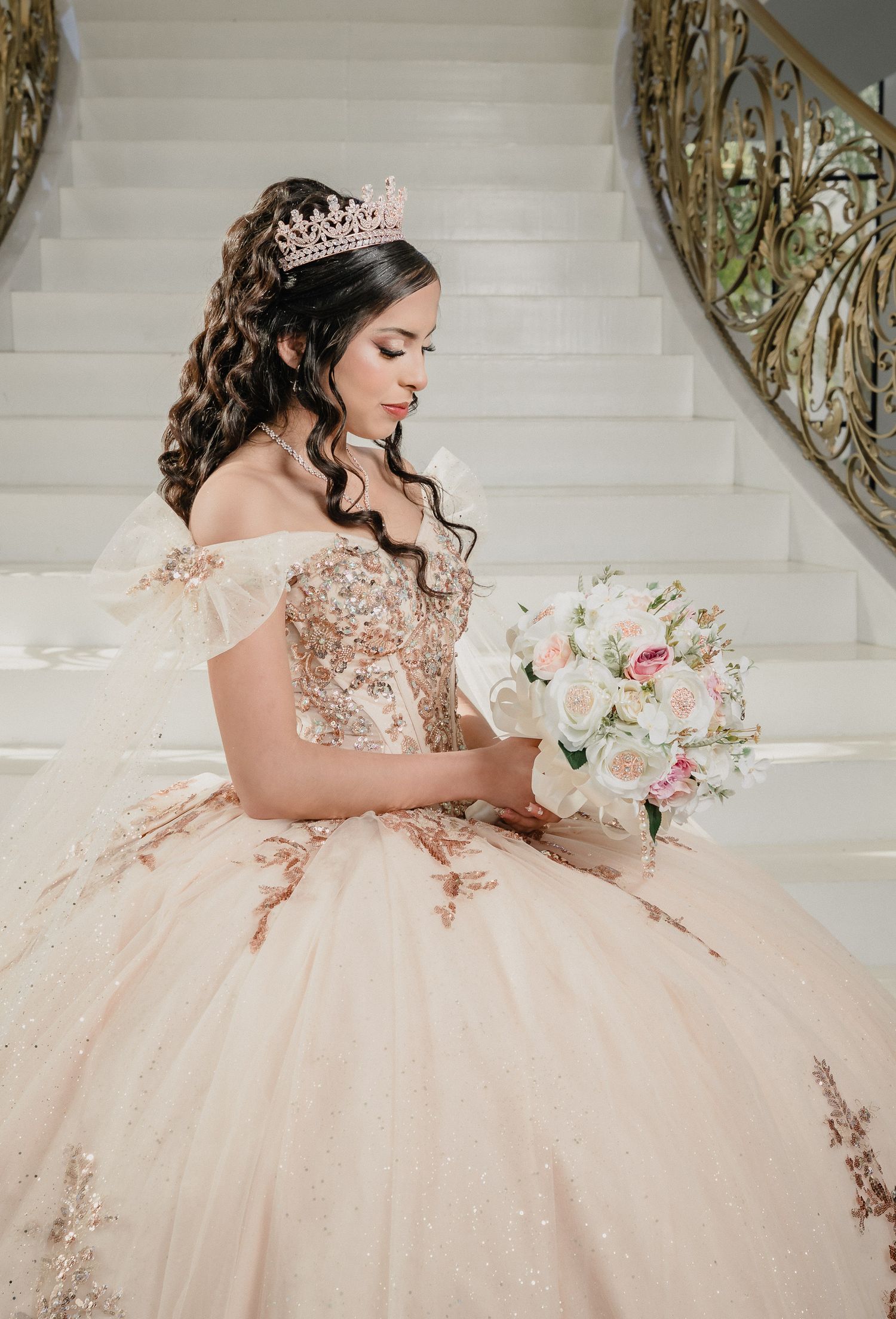 Elegant quinceañera gown in champagne with floral appliques and beading photographed on grand white staircase.
