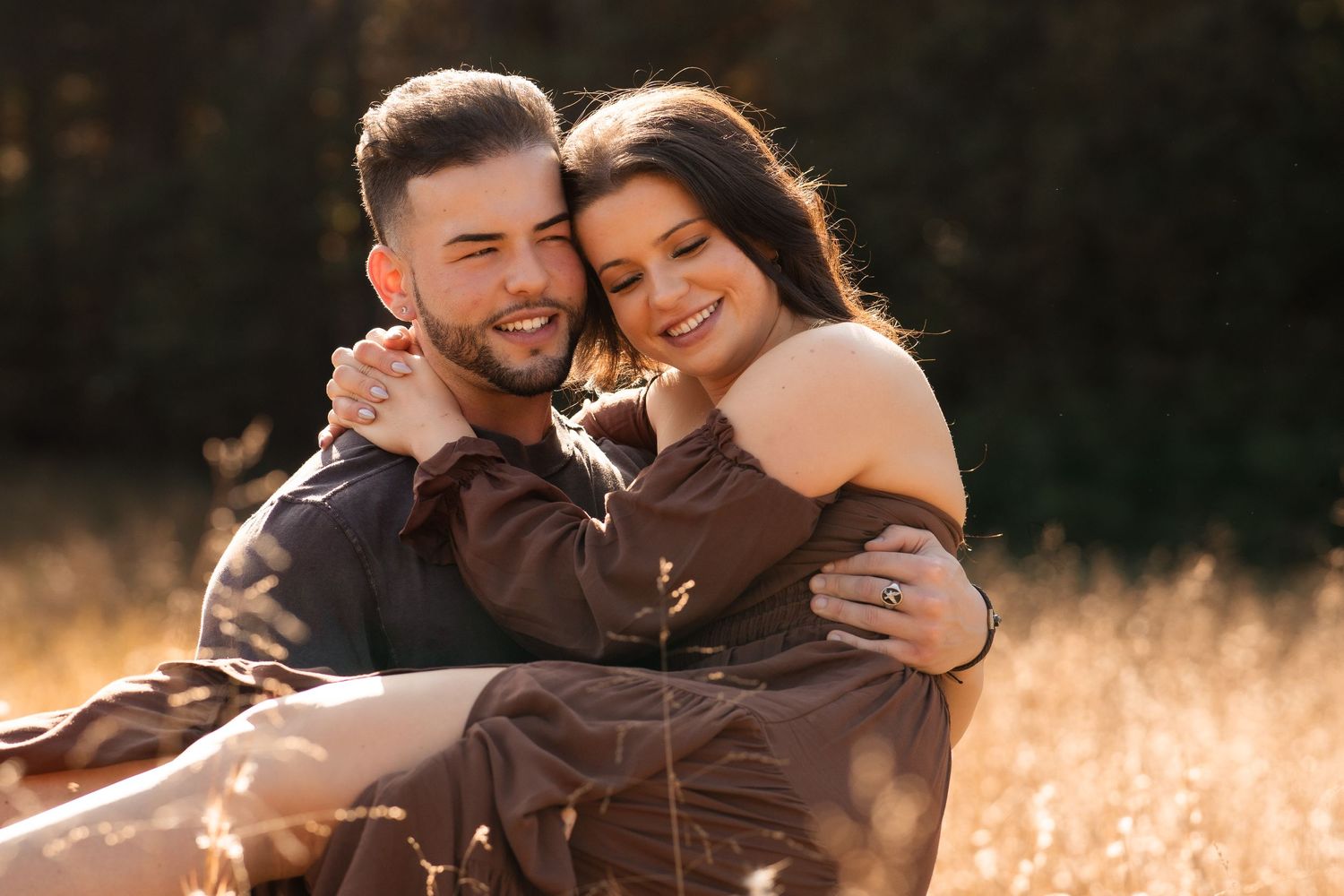 Couple sharing intimate moment while sitting in golden field during sunset.
