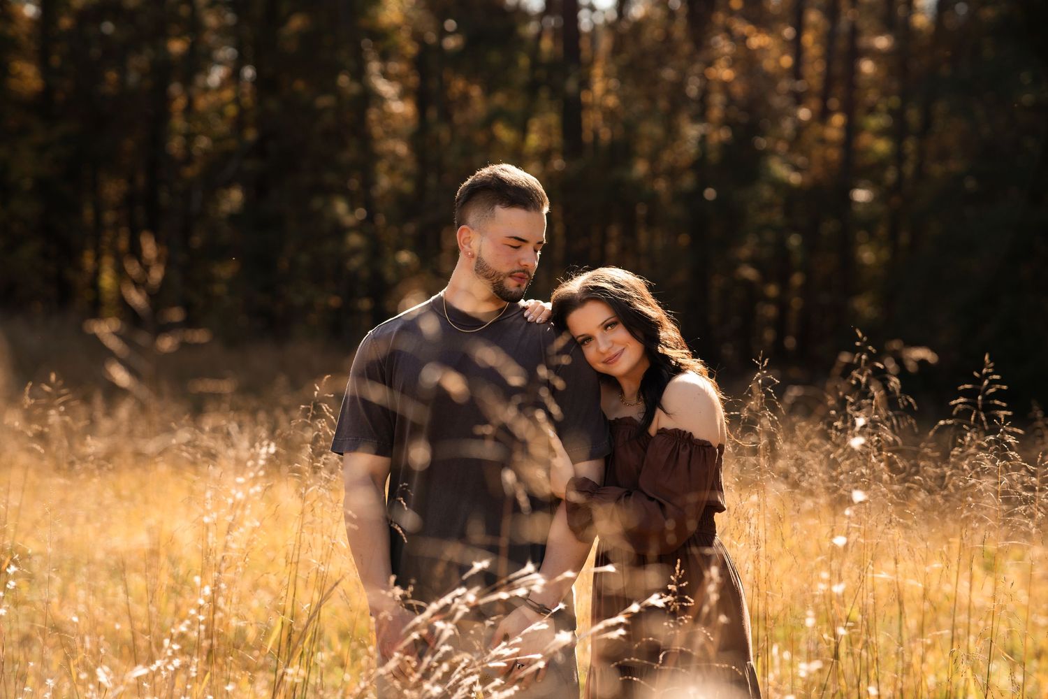 Couple in matching brown outfits embracing in autumn field at sunset.