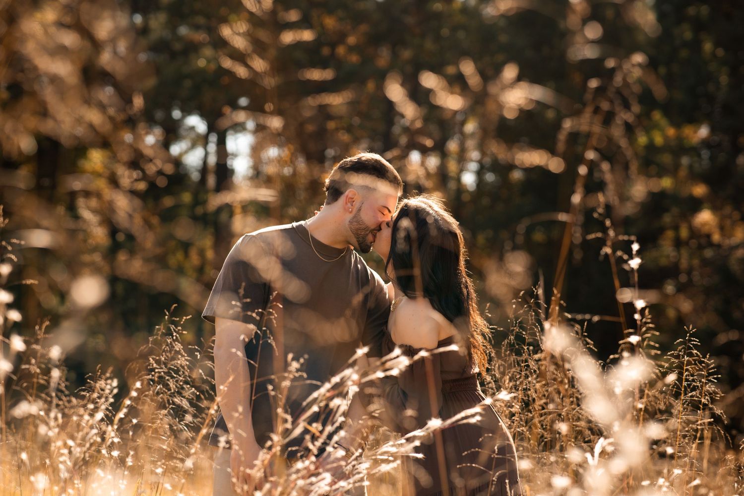 Couple in casual outfits sharing intimate moment in sunlit field.