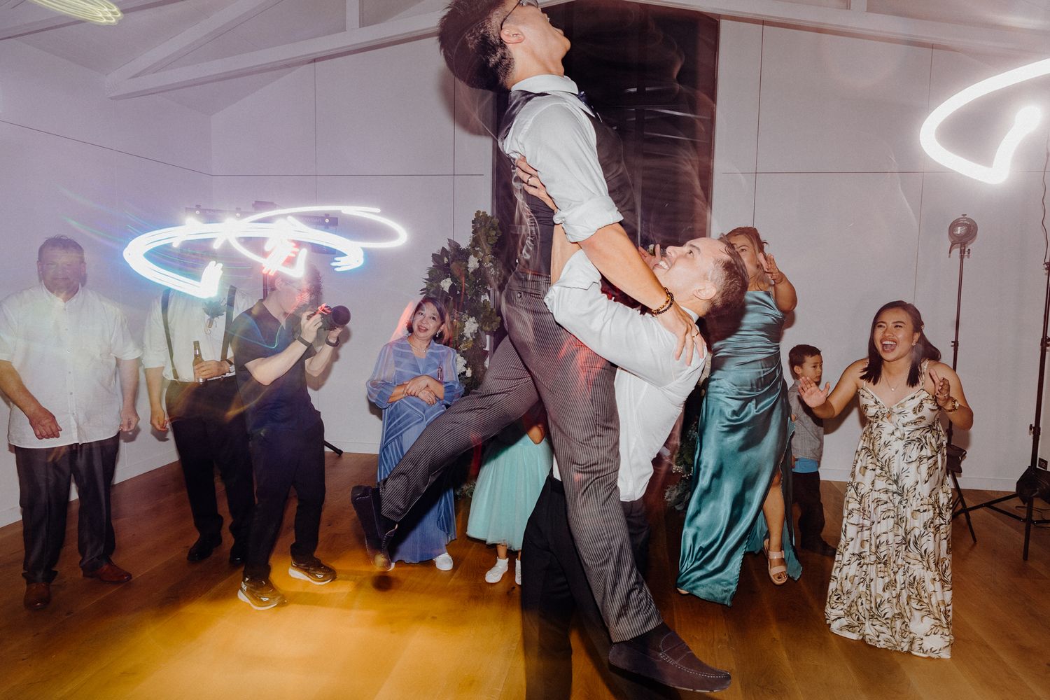 Lively wedding reception dancers move energetically on the dance floor captured by Apertured Media Auckland Wedding Photographer.