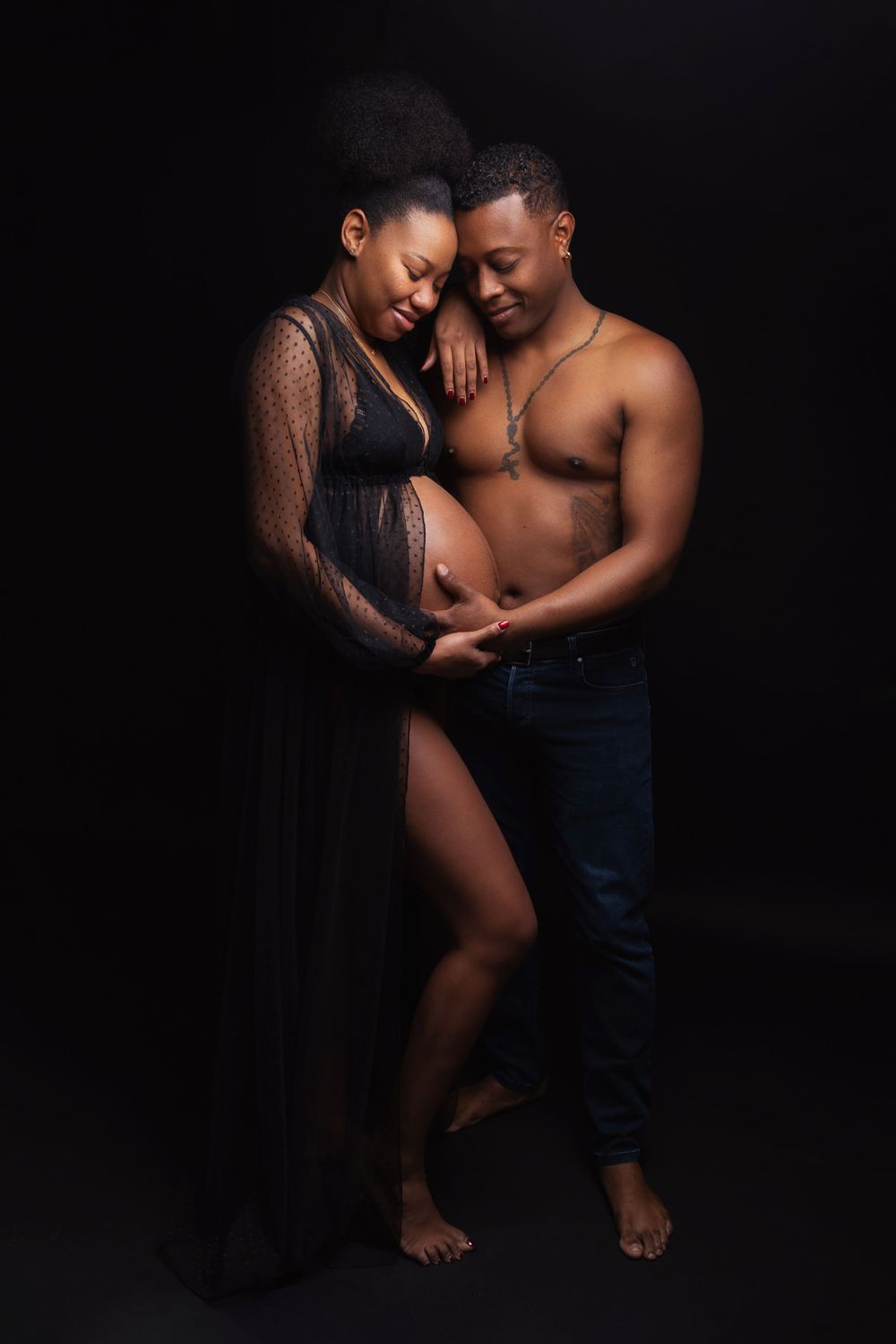 Intimate maternity photo showing a couple embracing in a dark studio setting with dramatic lighting.