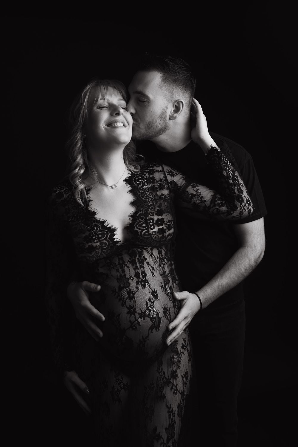 A romantic black and white portrait featuring an intimate couple embracing, with the woman wearing a delicate lace dress.