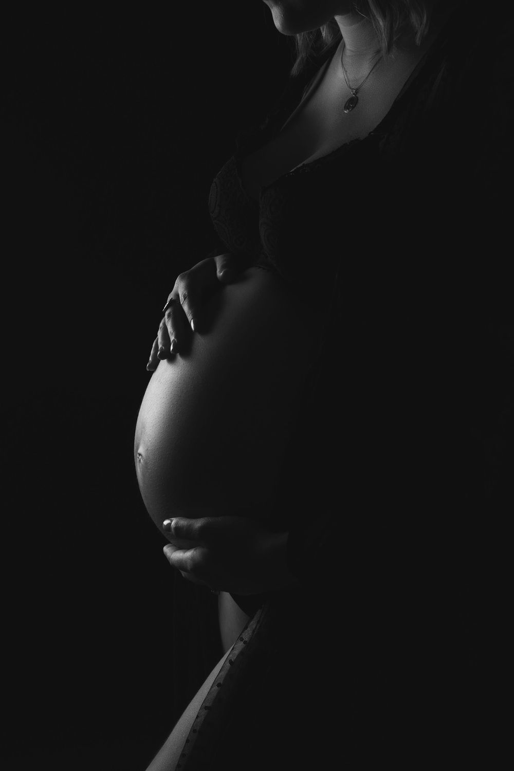 Artistic black and white silhouette shows a pregnant woman's belly in dramatic side profile lighting.