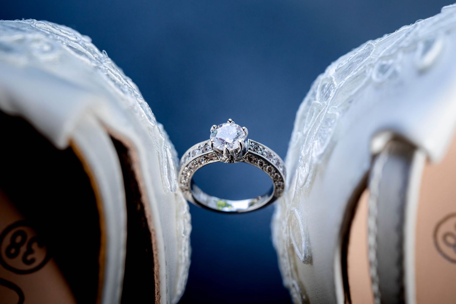 Diamond engagement ring artistically positioned between white bridal shoes.