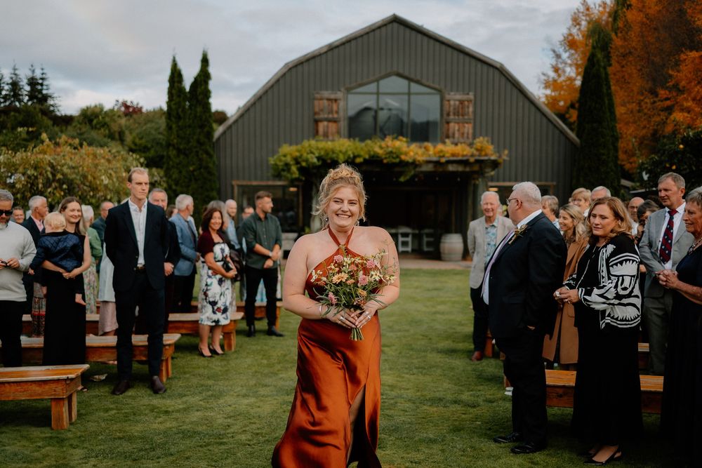 Fall wedding ceremony at a rustic barn venue with guest seating on wooden benches and vibrant autumn foliage.
