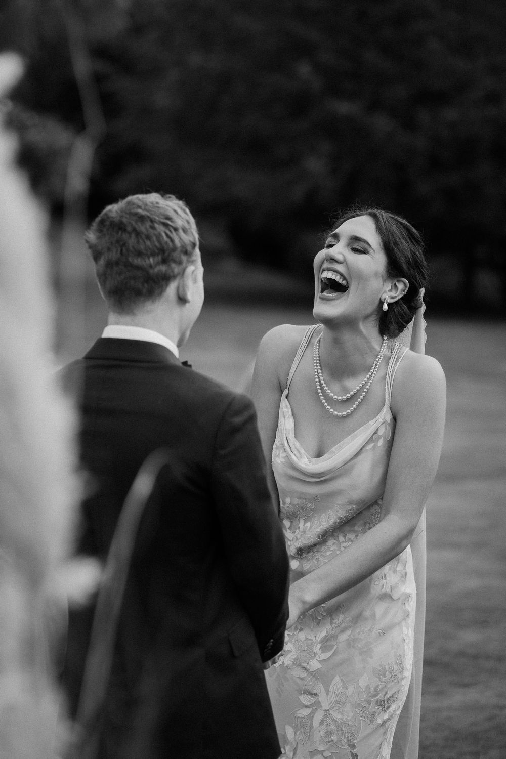 A candid black and white wedding moment shows the bride laughing joyfully during the ceremony.