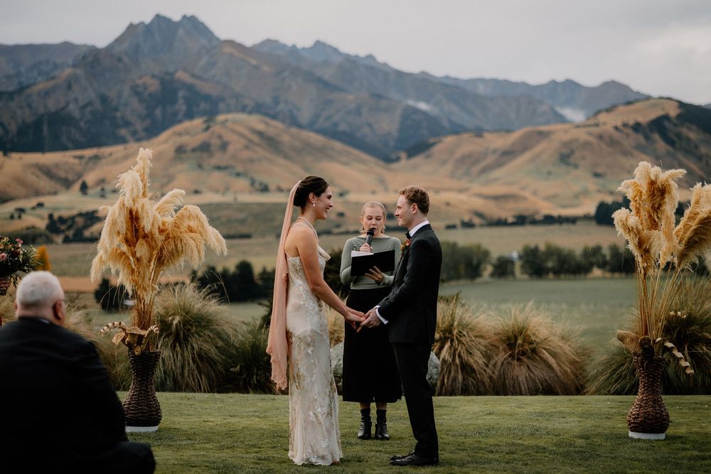 A wedding ceremony takes place outdoors with stunning mountain views and pampas grass decorations.